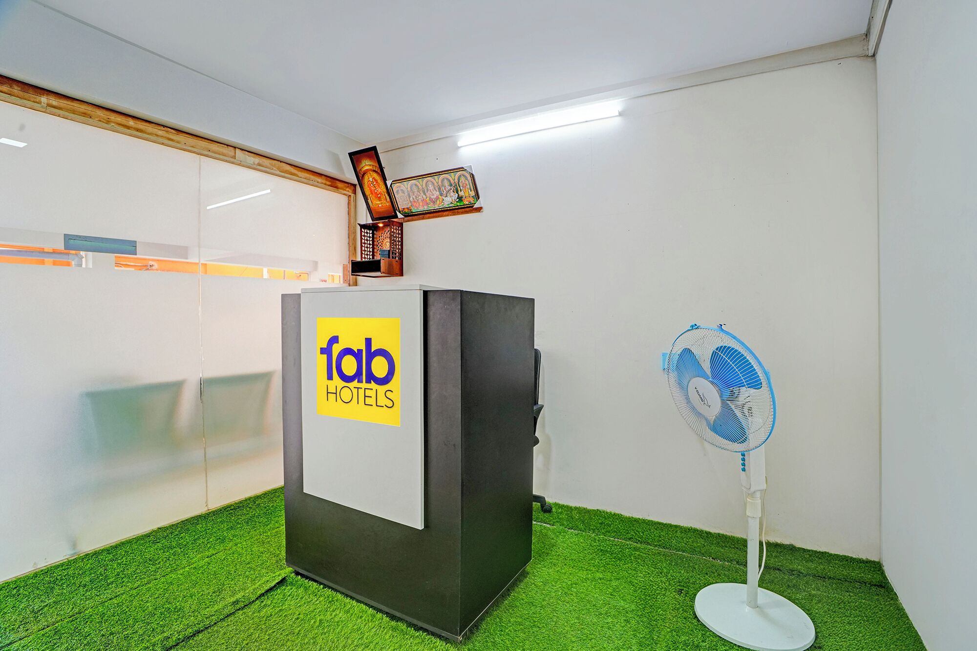 Ein Zimmer mit einer Rezeption mit der Aufschrift 'fab hotels', einem kleinen Ventilator und einer wandmontierten Lampe.