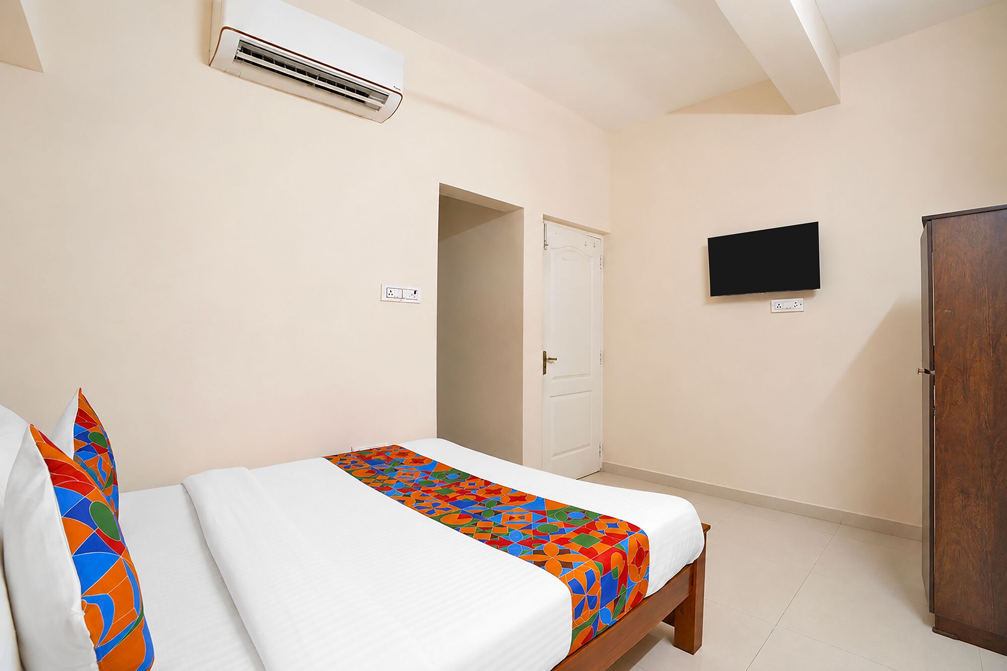A bedroom with a bed, a TV, a wardrobe, and an air conditioning unit.