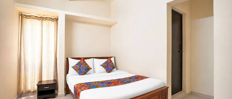 A bedroom with a bed, a nightstand, a door, and a window with curtains.