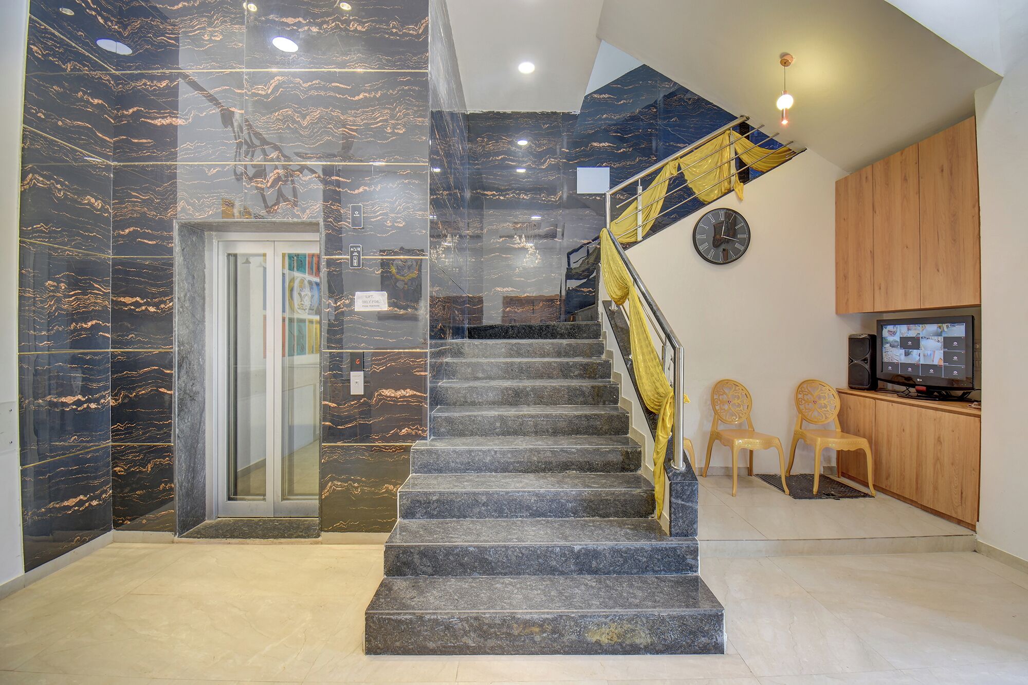 Un escalier aux murs de marbre, une horloge et un téléviseur dans un intérieur moderne.