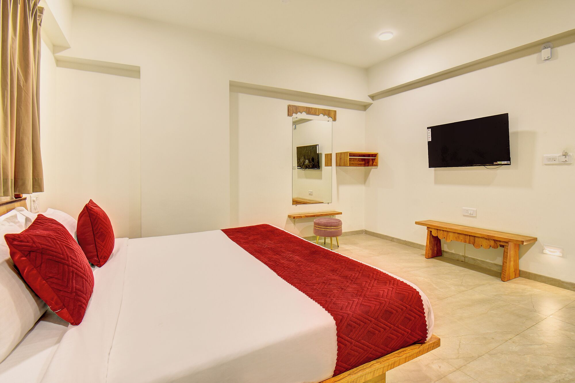 Habitació d'hotel amb un llit, televisió, mirall i una petita banca de fusta.