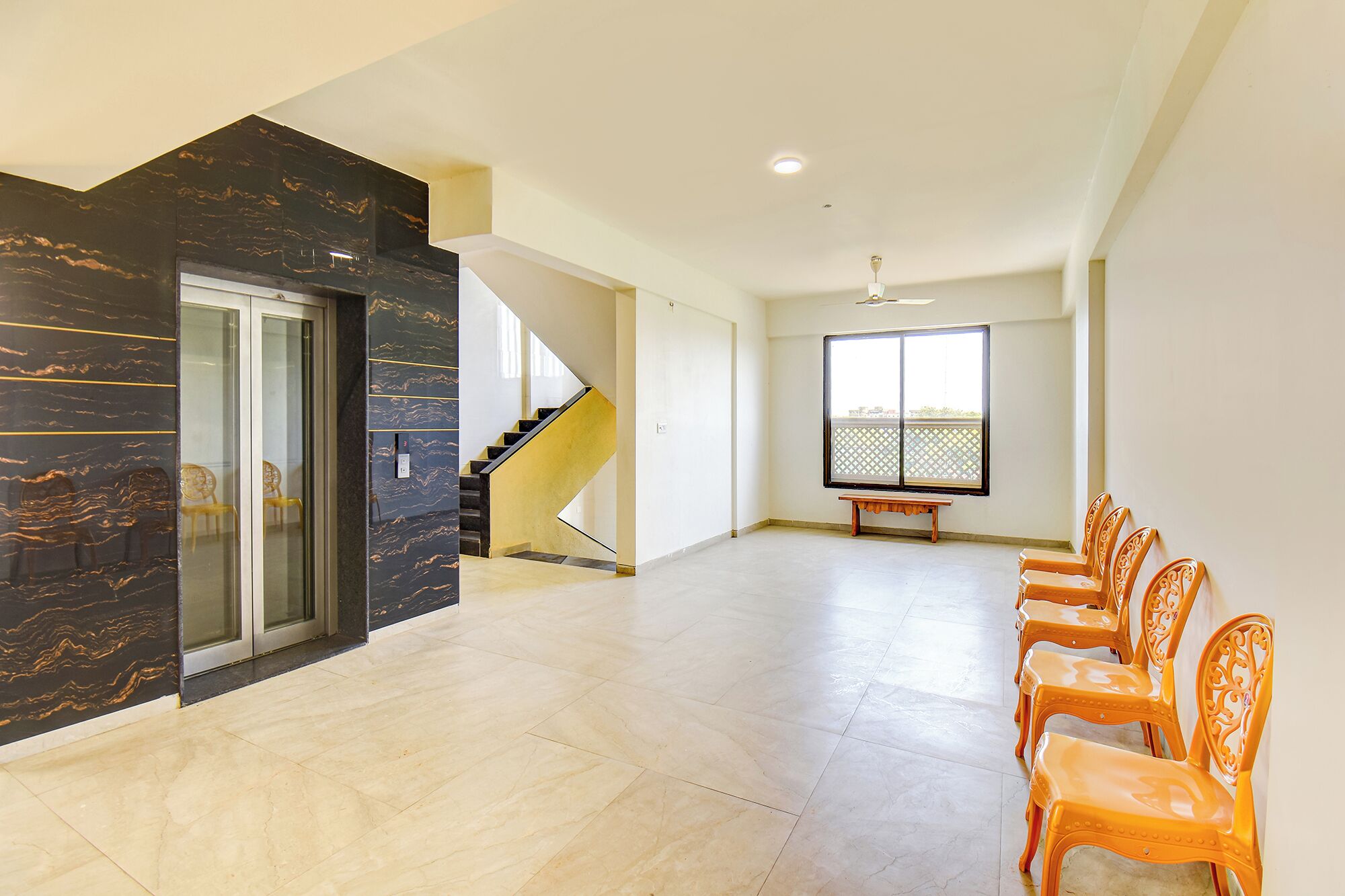 A spacious room with a staircase, a bench, and a row of chairs.