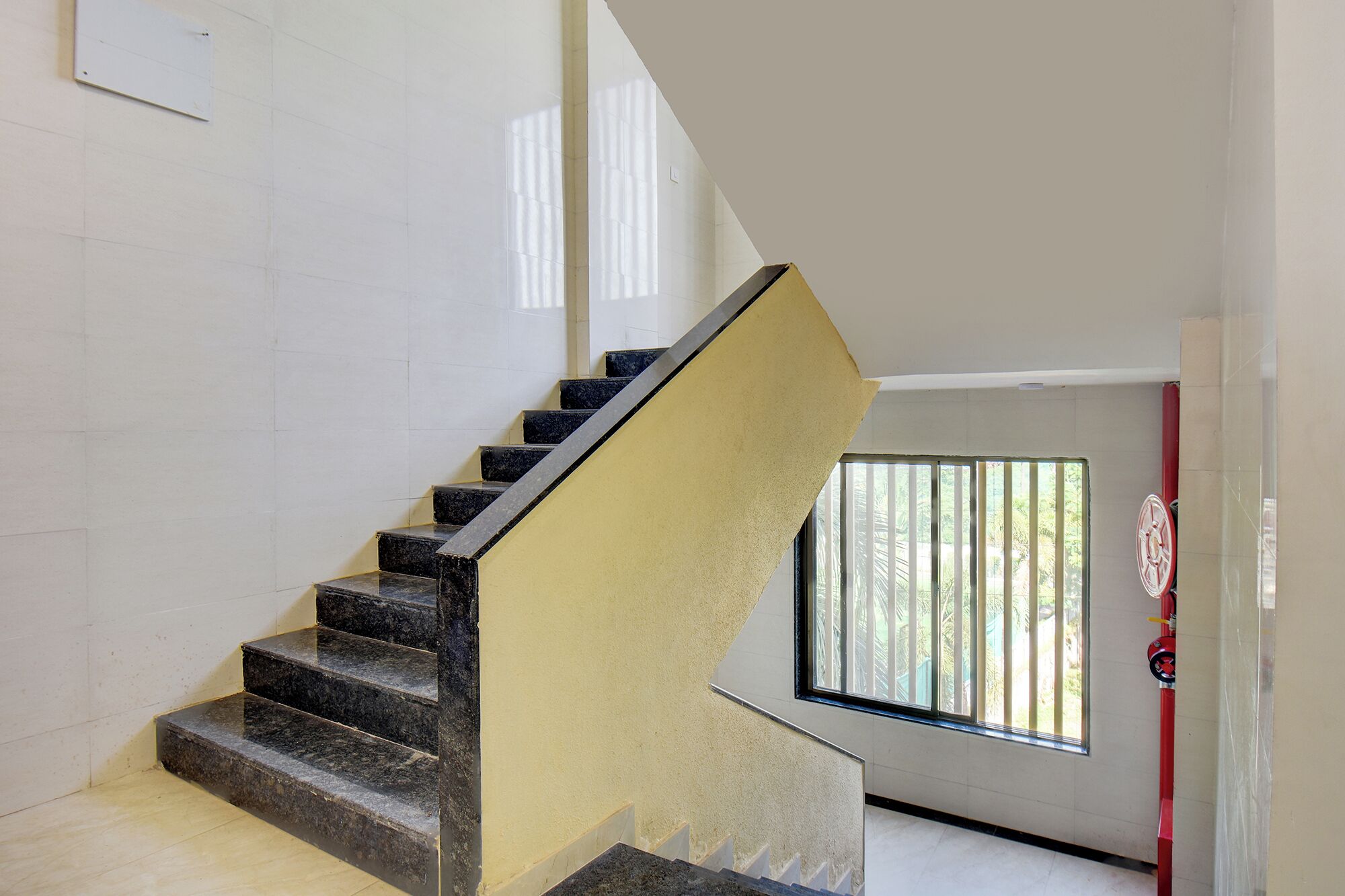 A staircase with black steps and a yellow handrail, leading to a room with a window and a red door.