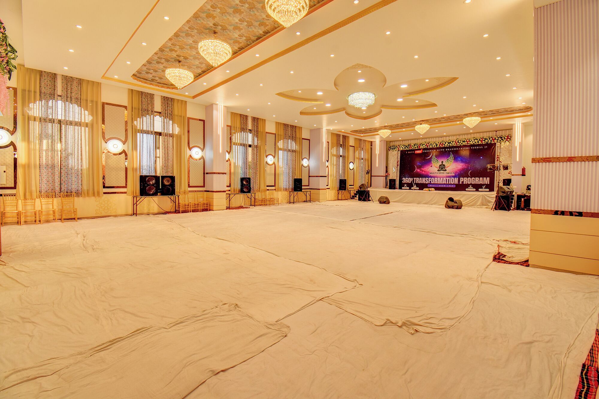 A large, well-lit hall with a stage, chandeliers, and a banner for a transformation program.