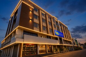 Un hotel de varios pisos con un llamativo letrero 'fab hotels', un escaparate visible con el rótulo 'JOYBEAN' y un diseño arquitectónico moderno con líneas iluminadas.