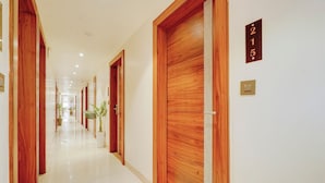 Un couloir d’hôtel avec des portes en bois, des panneaux indiquant le numéro des chambres et des plantes en pot.
