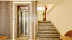 Un hall d’entrée moderne avec un sol en marbre, un comptoir d’accueil, un escalier et une plante en pot.