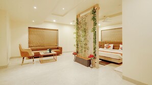 Une chambre d’hôtel avec un canapé, une petite table avec un plateau, une plante décorative et un lit avec des oreillers.