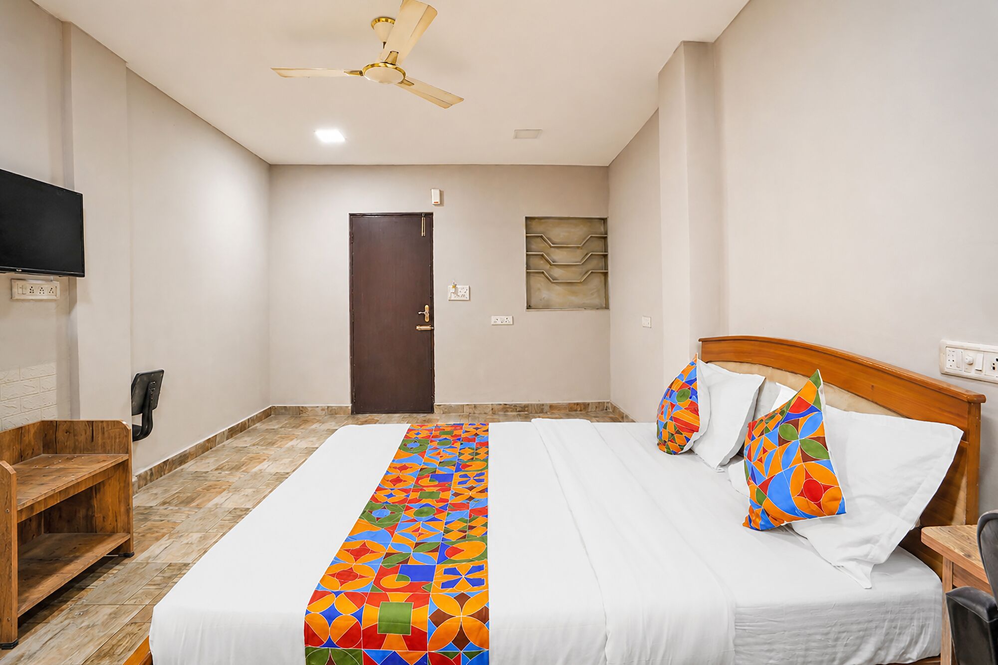 A hotel room with a bed, a wooden nightstand, a TV, a ceiling fan, and a door.