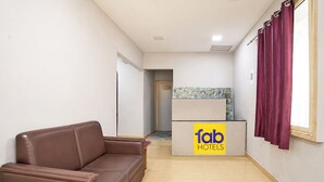 A hotel reception area with a brown leather sofa, a reception desk labeled 'fab HOTELS,' and a window with curtains. - Fabhotel Moon Stay - Nr Urappakkam Railway Station (Chennai)