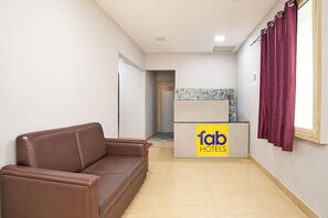 Uma área de recepção de hotel com um sofá de couro marrom, um balcão de recepção com a inscrição 'fab HOTELS' e uma janela com cortinas.