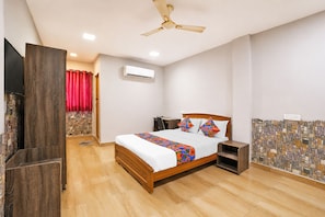 Quarto com cama de madeira, escrivaninha, cadeira, ventilador de teto e parede com padrão de pedra.