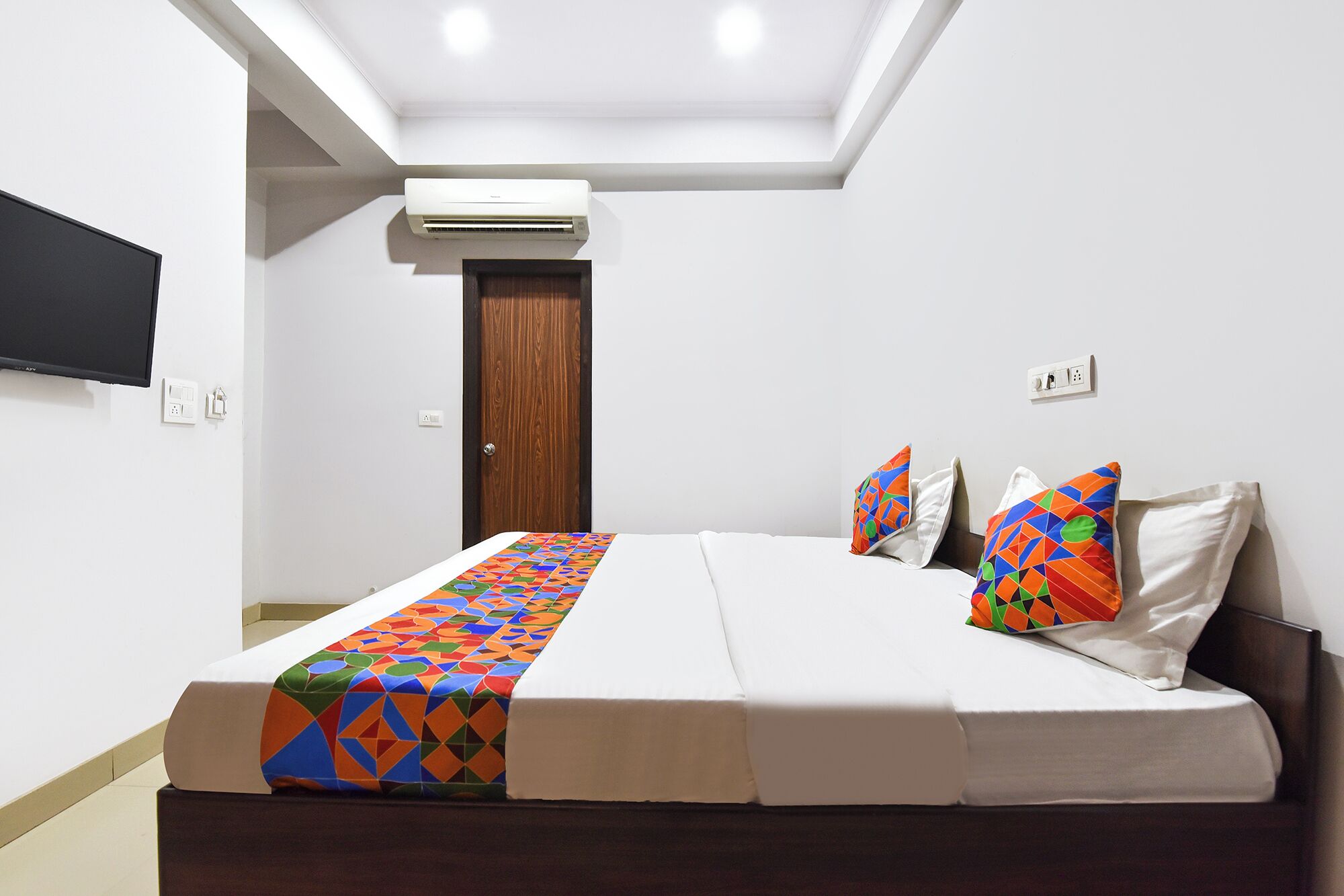 Una habitación de hotel con una cama, televisión, aire acondicionado y una puerta.