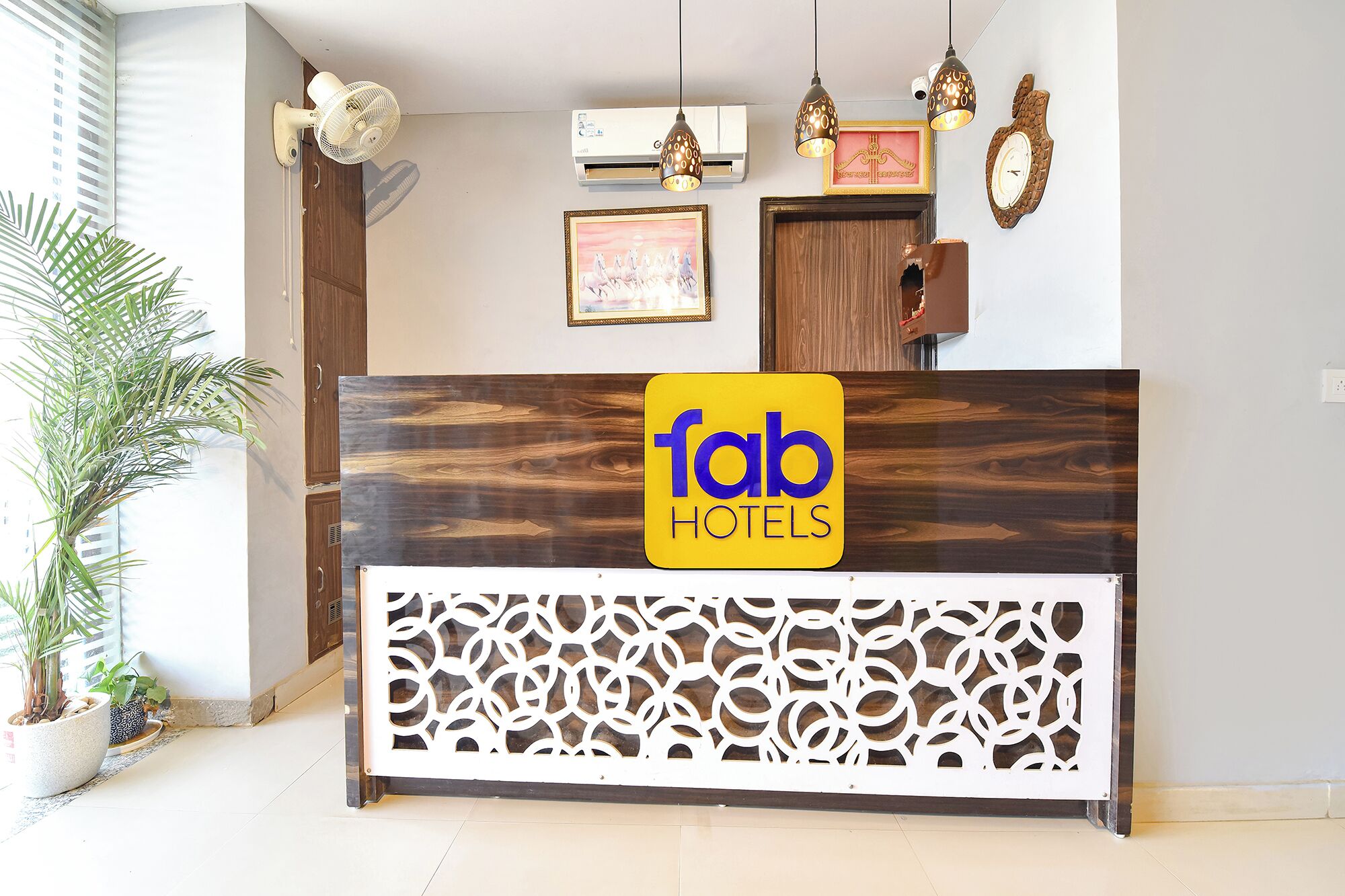 A reception desk with a wooden finish, a 'fab hotels' sign, and a decorative white panel.
