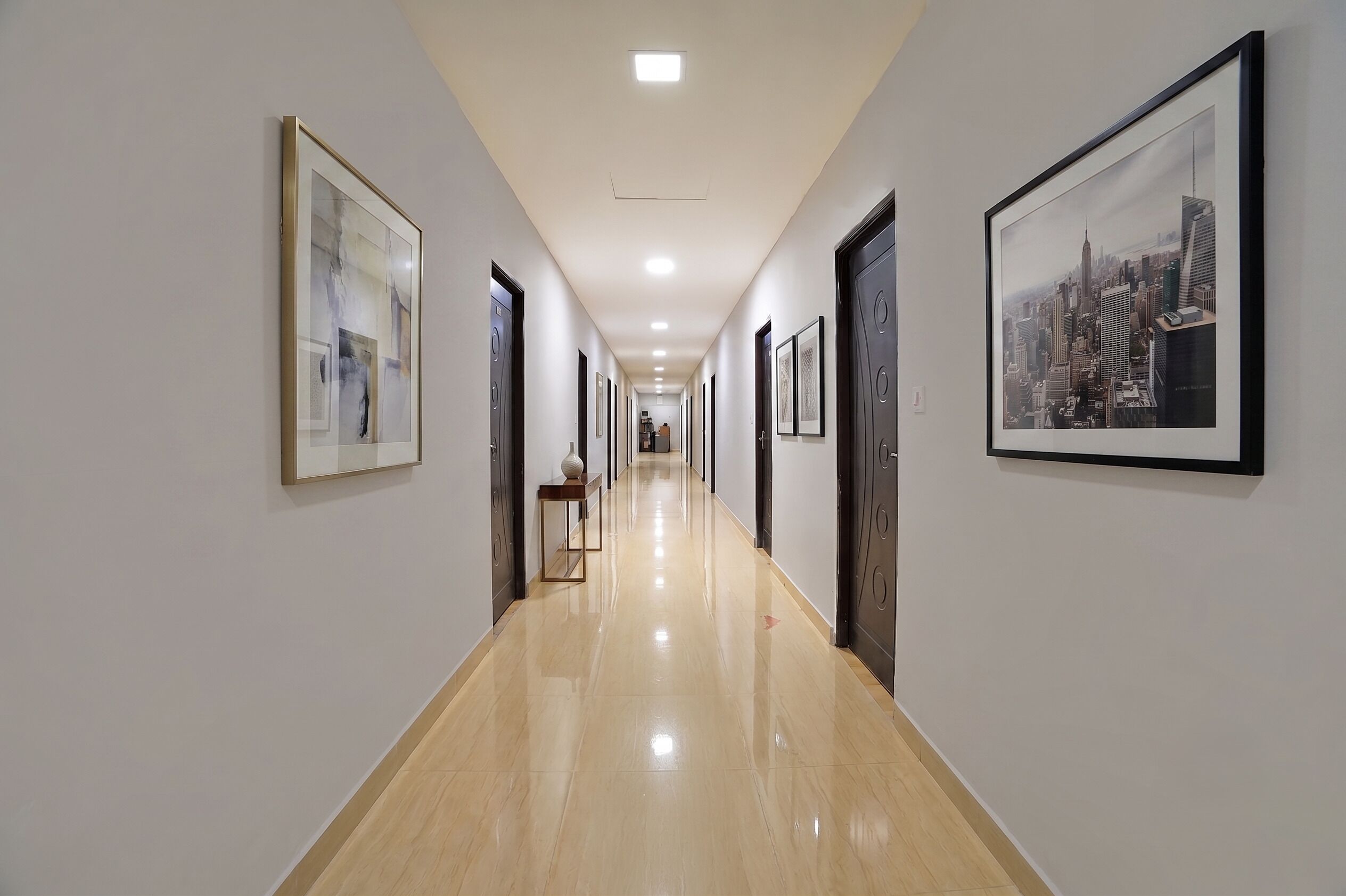 Un pasillo con obras enmarcadas en las paredes, suelo pulido y puertas que dan a habitaciones.