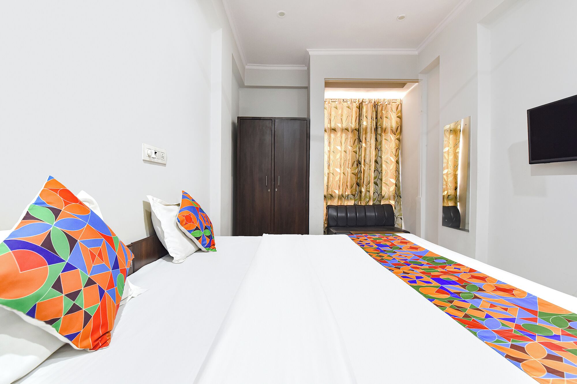 A hotel room with a bed, a desk, a chair, a TV, and a window with curtains.