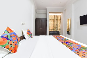 Una habitación de hotel con cama, escritorio, silla, televisor y ventana con cortinas.