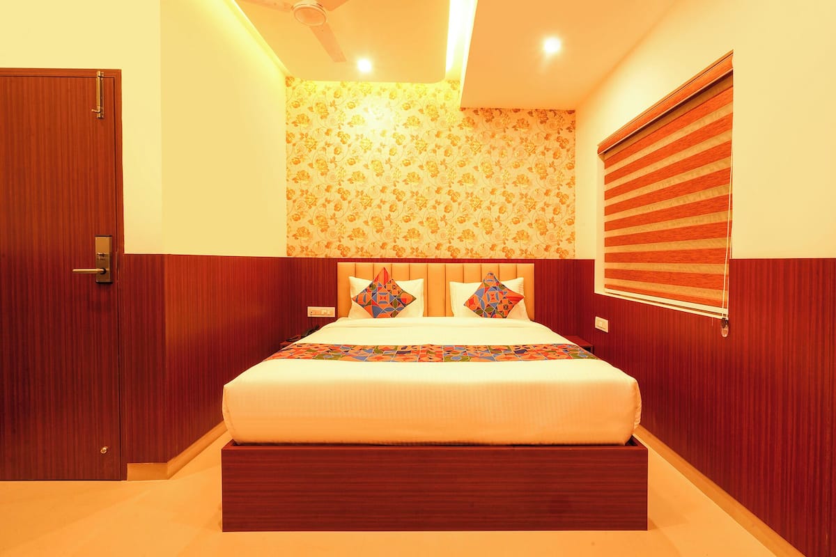 Quarto com cabeceira de madeira, cama com almofadas estampadas, porta de madeira e janela com persianas.