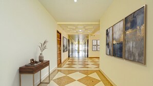 A hallway with a checkered floor, framed artwork on the walls, and a console table with decorative items. - Fabhotel New Raadhey Guest Inn (Nellore)