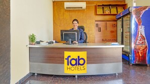 A reception desk at a hotel with a logo, a computer, a plant, and a refrigerator. - Fabhotel New Raadhey Guest Inn (Nellore)
