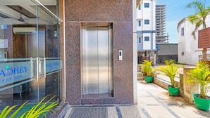 A hotel entrance with a glass door, a metal elevator, and potted plants outside. - Fabhotel New Raadhey Guest Inn (Nellore)