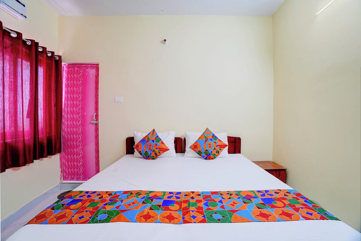 A hotel room with a bed, pillows, a curtain, and a wall-mounted air conditioner.