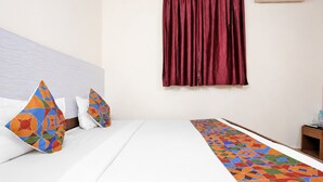 Une chambre d’hôtel avec un lit, des oreillers, un couvre-lit à motifs, une fenêtre avec des rideaux et une table de chevet sur laquelle se trouve une bouteille.