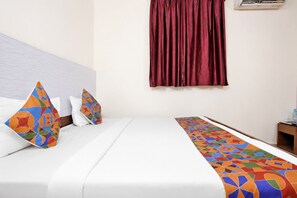 Habitación de hotel con cama, almohadas, un corredor de cama estampado, una ventana con cortinas y una mesita de noche con una botella.