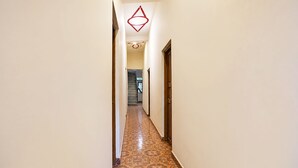 Un couloir étroit au sol décoré de motifs, une porte en bois sur la droite et un escalier au fond.
