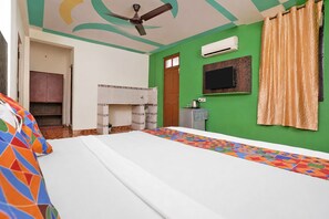 Un dormitorio con cama, ventilador de techo, televisión y pared verde.