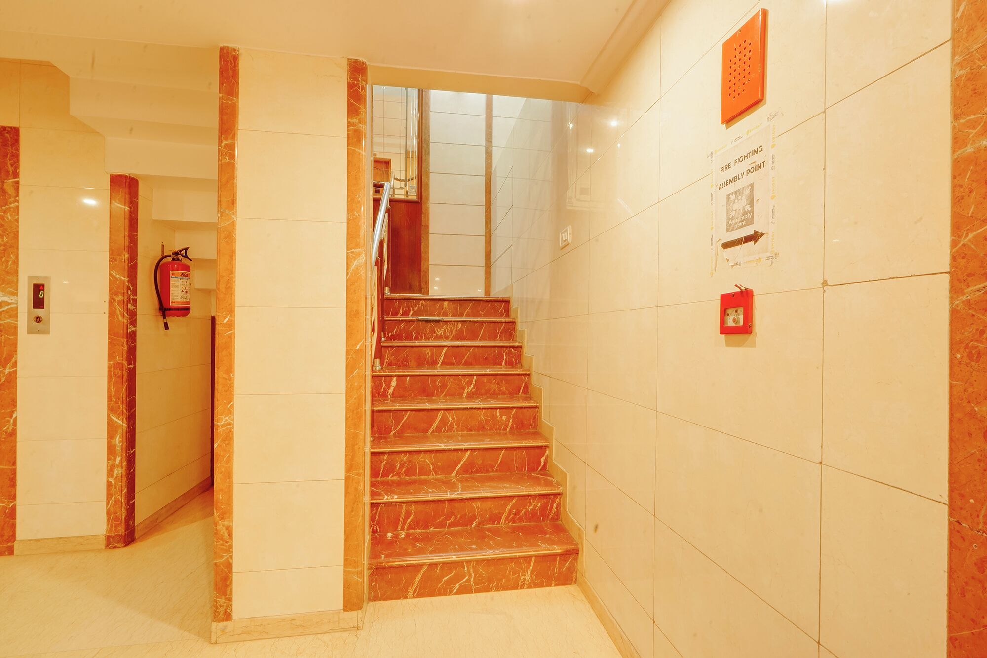 A marble staircase with a fire extinguisher and emergency exit sign on the wall.