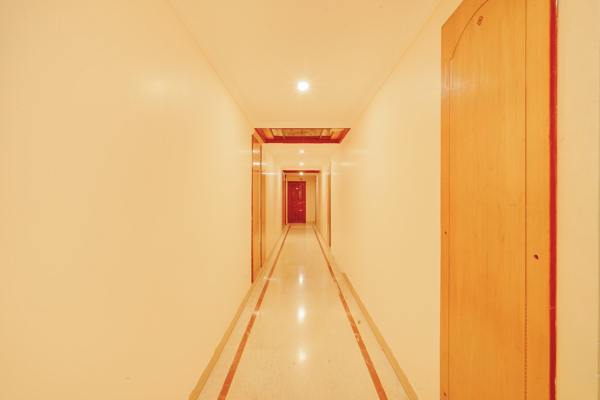 Ein Flur mit einer Holztür rechts, einer roten Tür am Ende und einer Leuchte an der Decke.