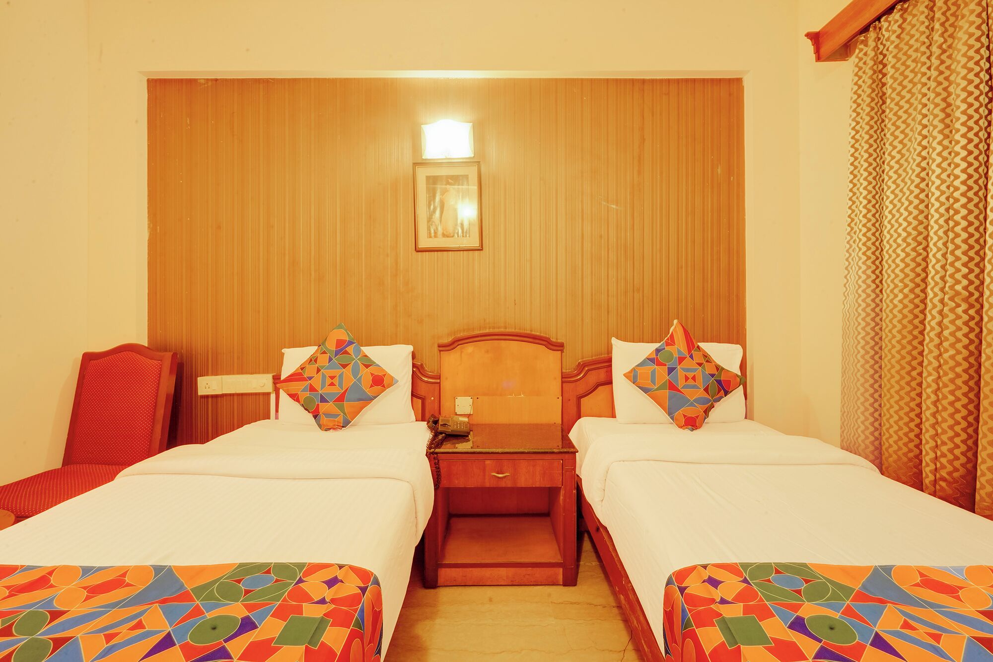 A hotel room with two beds, a wooden headboard, a nightstand, and a single light fixture.