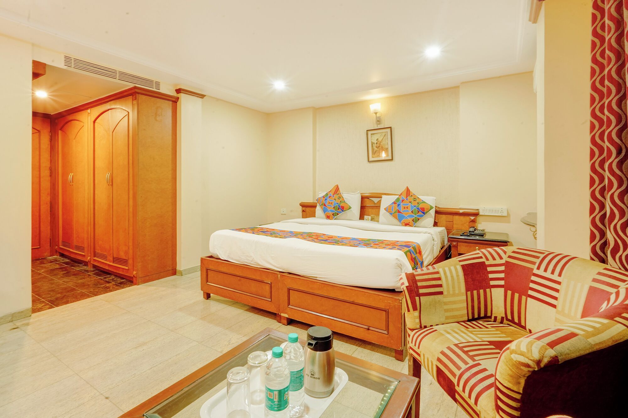 A hotel room with a bed, a chair, a bedside table, and a tray with bottles.