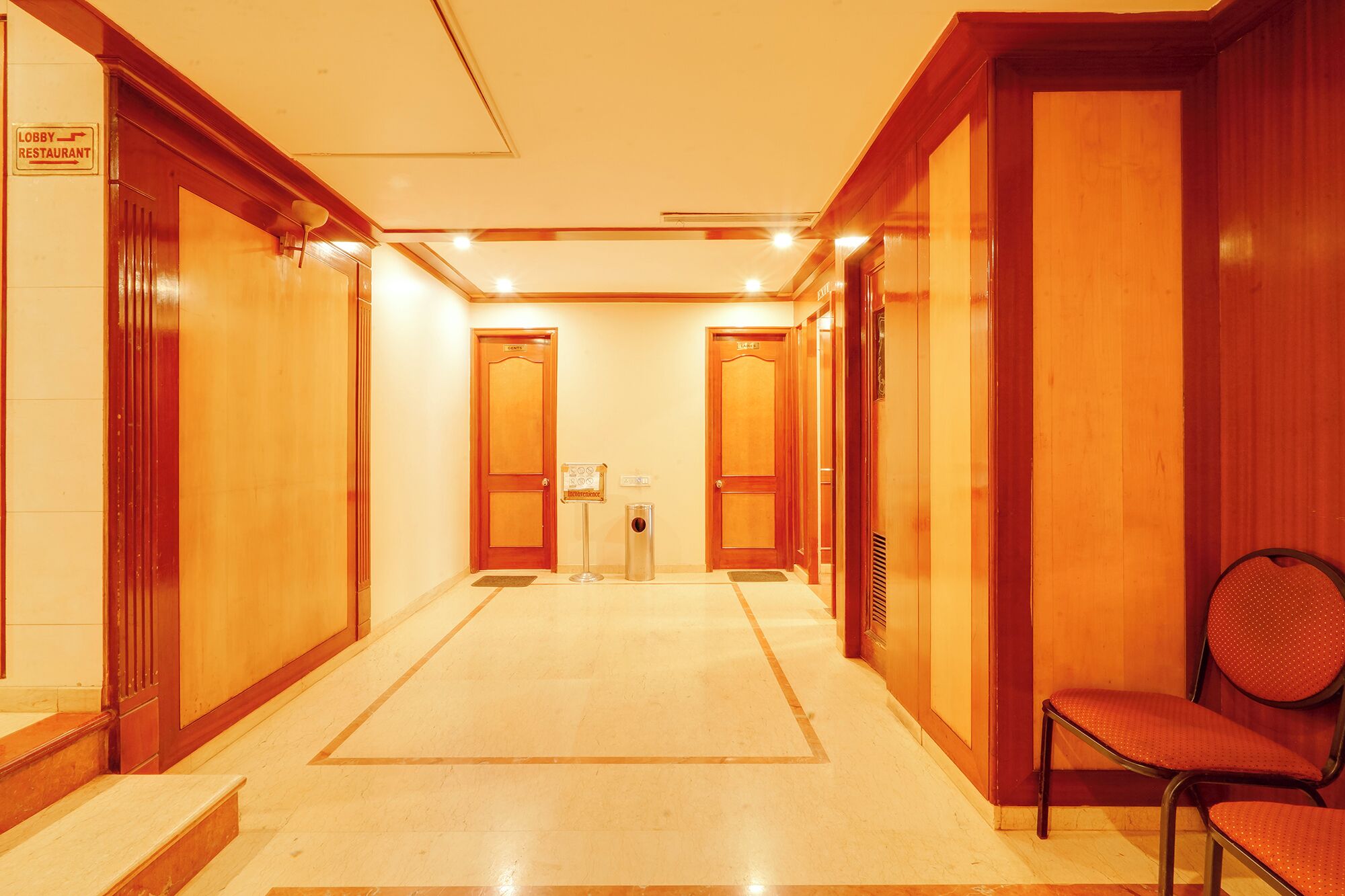 A hotel lobby with a central reception desk, a waiting area with a chair, and multiple doors leading to guest rooms.