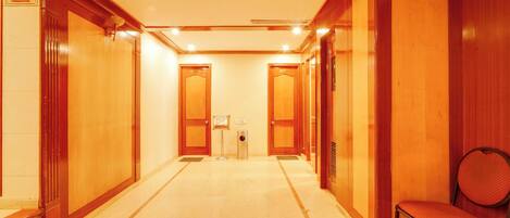 A hotel lobby with a central reception desk, a waiting area with a chair, and multiple doors leading to guest rooms.