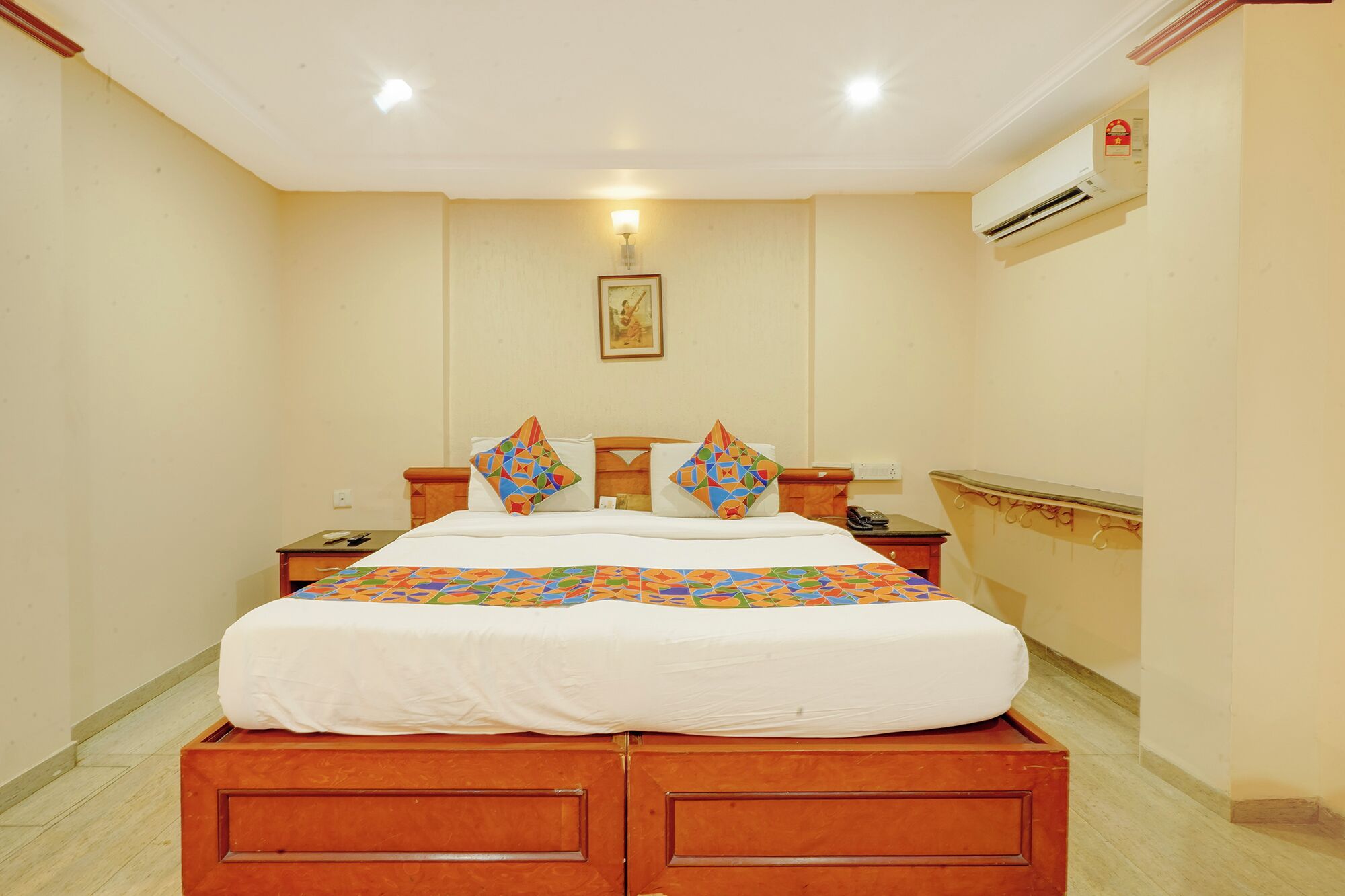 A hotel room with a bed, two nightstands, a wall-mounted air conditioner, and a framed picture on the wall.