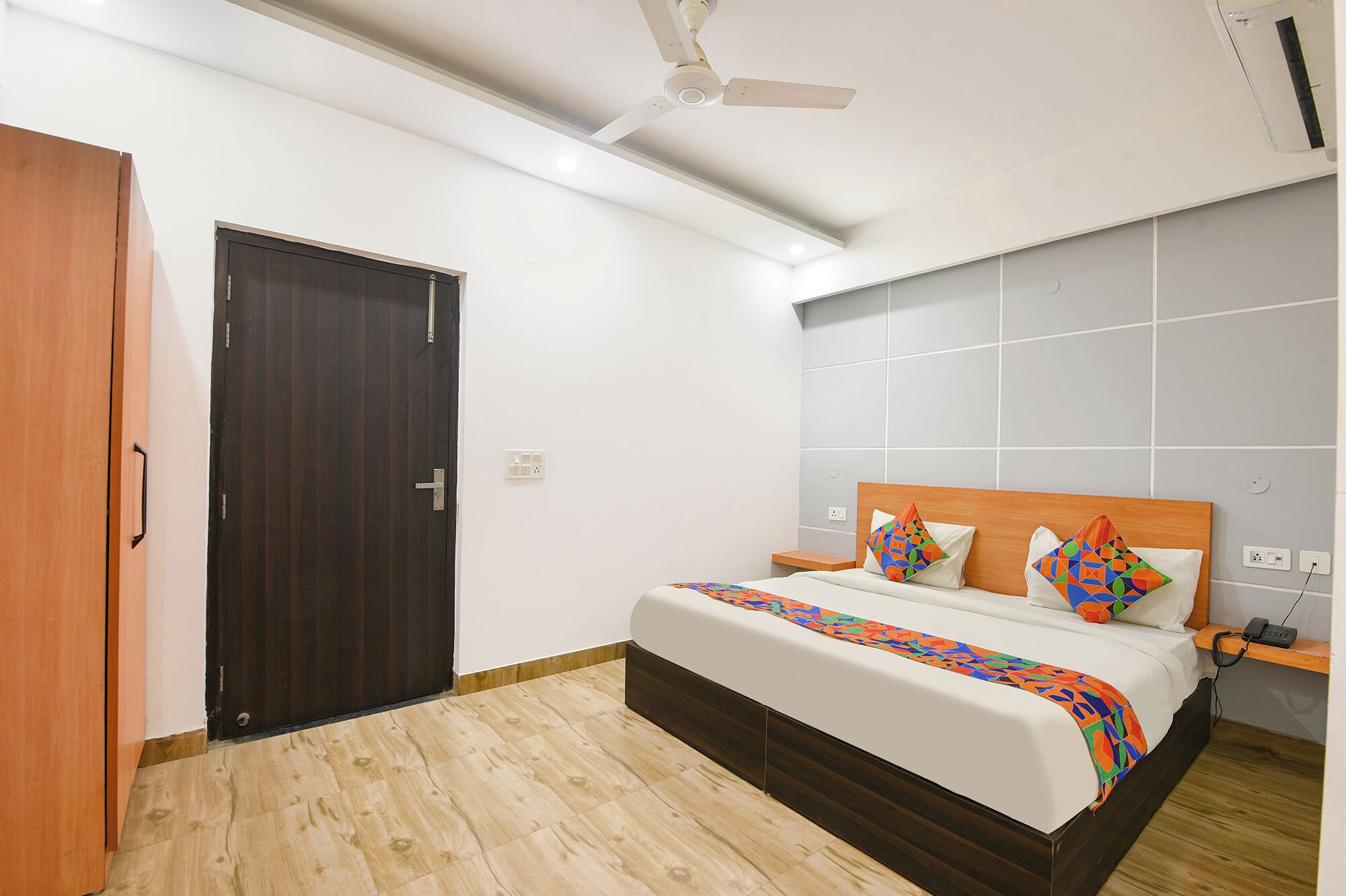 A bedroom with a bed, a wooden door, a ceiling fan, and a tiled wall.