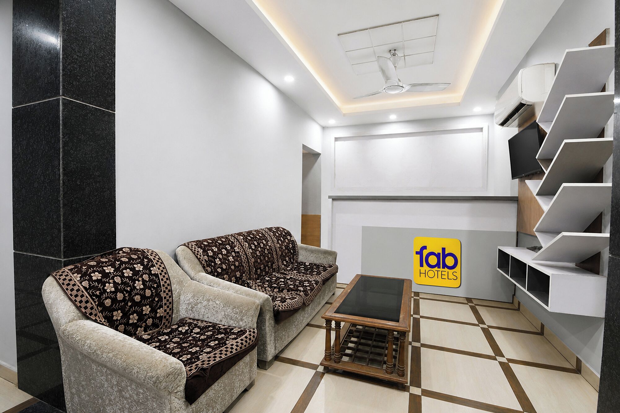 Eine moderne Lobby mit zwei gemusterten Sesseln, einem kleinen Holztisch, einer Treppe und einem Schild mit 'fab hotels'.