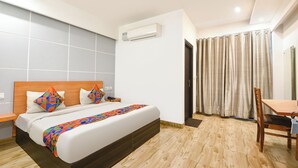 A hotel room with a bed, a desk, a chair, an air conditioning unit, and a ceiling fan. - FabHotel A V Homes - Navjeevan Hospital & Maternity Centre (Gurugram)
