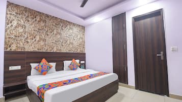 A bedroom with a bed, a ceiling fan, a wardrobe, and a wall with a geometric pattern.