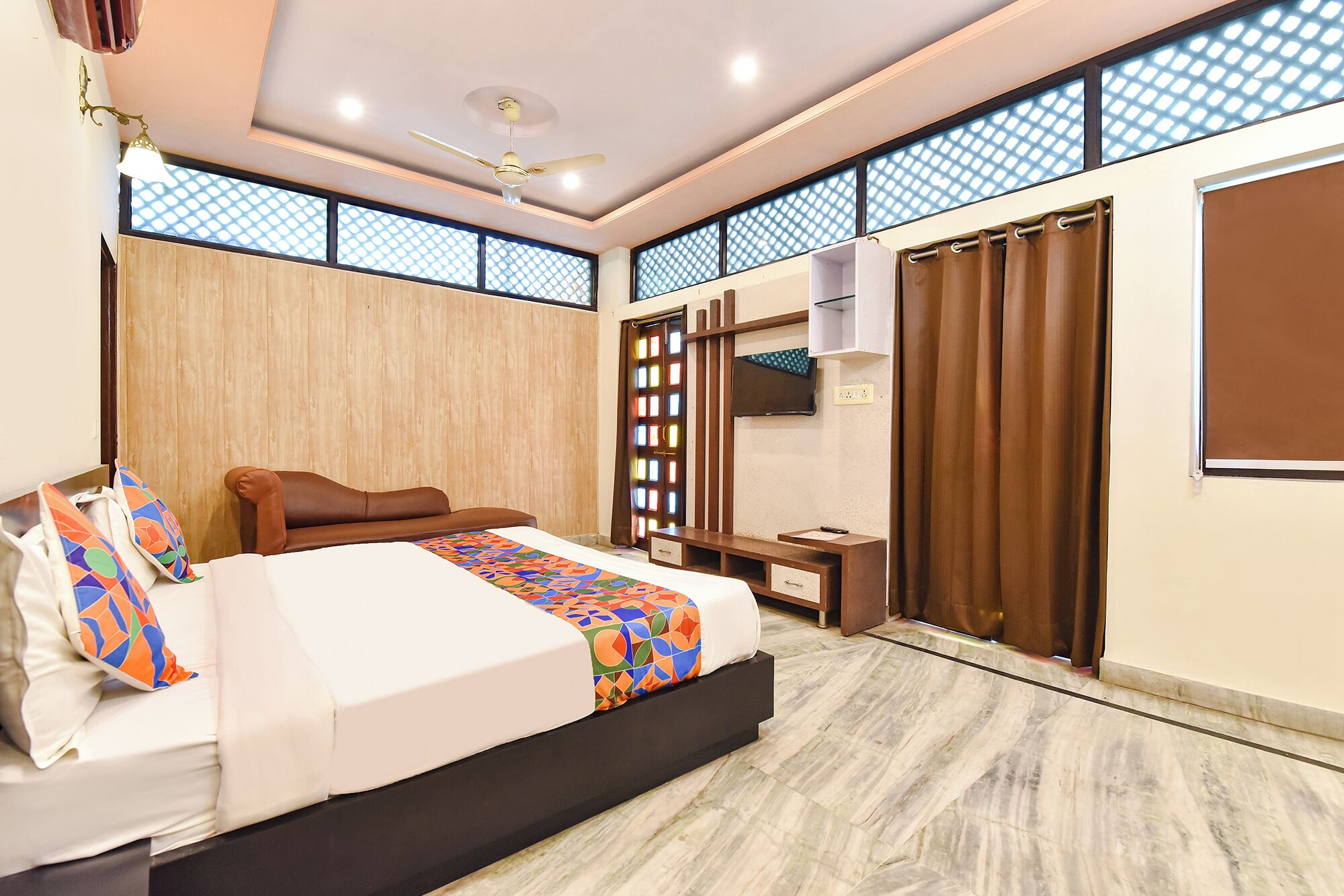 Un dormitorio con cama, escritorio, televisor y ventana con cortinas.