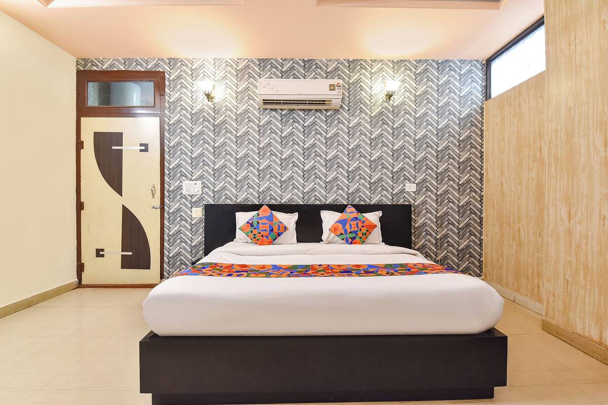 A modern bedroom with a herringbone-patterned wall, a bed with a geometric-patterned bedspread, and a built-in air conditioning unit.