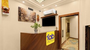 A hotel reception desk with a 'Tab Hotels' sign, a mounted television, a potted plant, and a wall-mounted security camera. - Fabhotel Vatsa Residency (Varanasi)