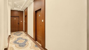 A hallway with wooden doors, a marble-patterned floor, and recessed ceiling lighting. - Fabhotel Vatsa Residency (Varanasi)