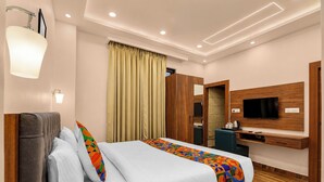 A hotel room with a bed, a TV, a wooden wardrobe, and a mirror. - Fabhotel Vatsa Residency (Varanasi)