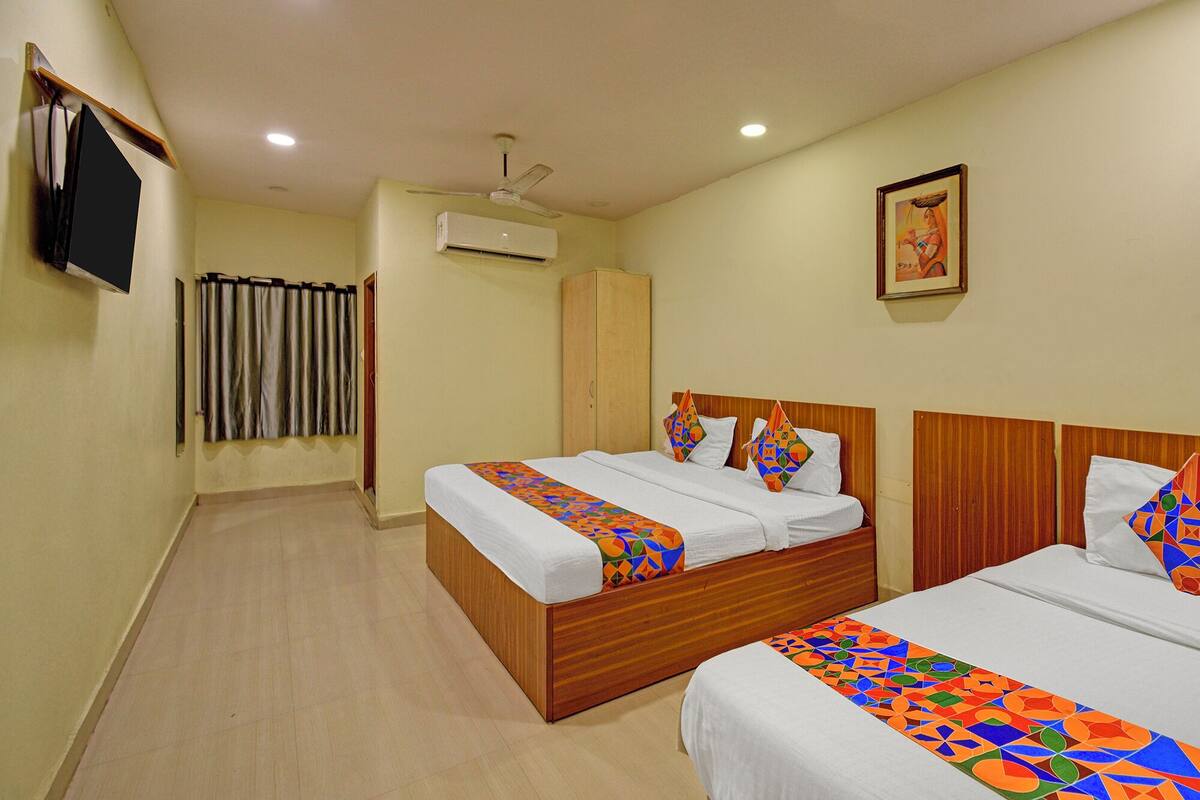 A hotel room with two beds, a TV, an air conditioner, a wardrobe, and a painting on the wall.