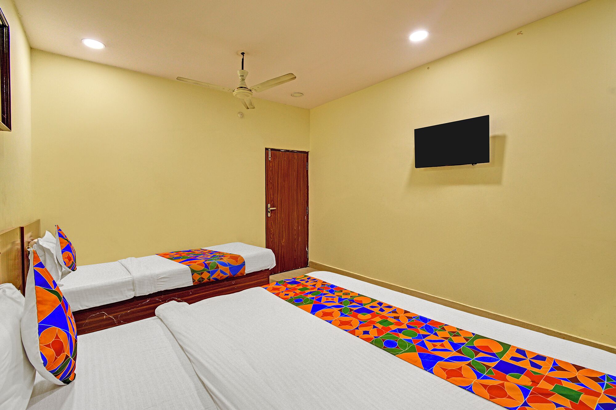 A hotel room with two beds, a ceiling fan, a TV, and a door.