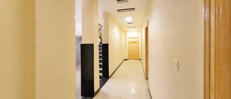 A hotel hallway with a marble floor, a staircase, and a door at the end.