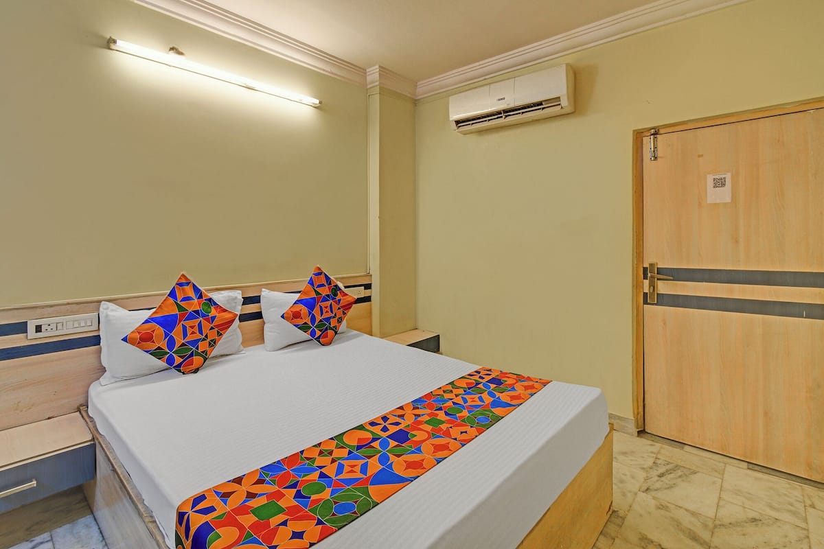 A hotel room with a bed, a nightstand, an air conditioning unit, and a wooden door.